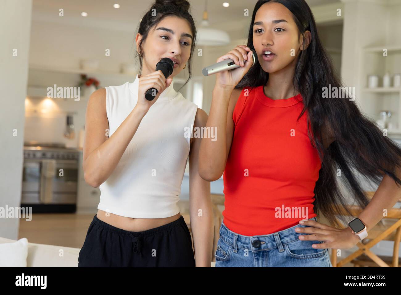 Diverse amiche che cantano karaoke nella cucina a pianta aperta, con microfoni wireless Foto Stock