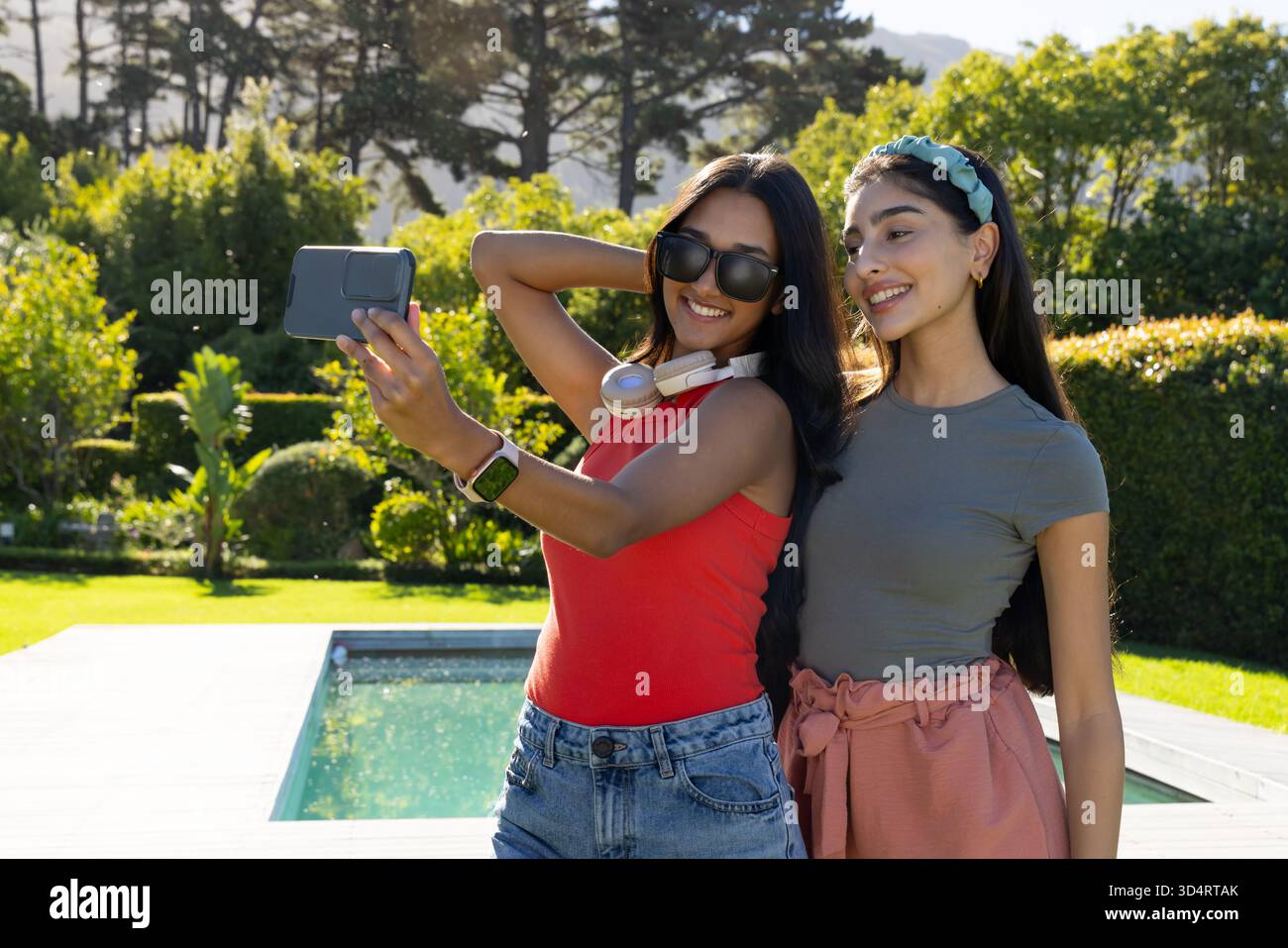 Scatta selfie con diverse amiche in piedi sul ponte della piscina sul retro, con smartphone e cuffie Foto Stock