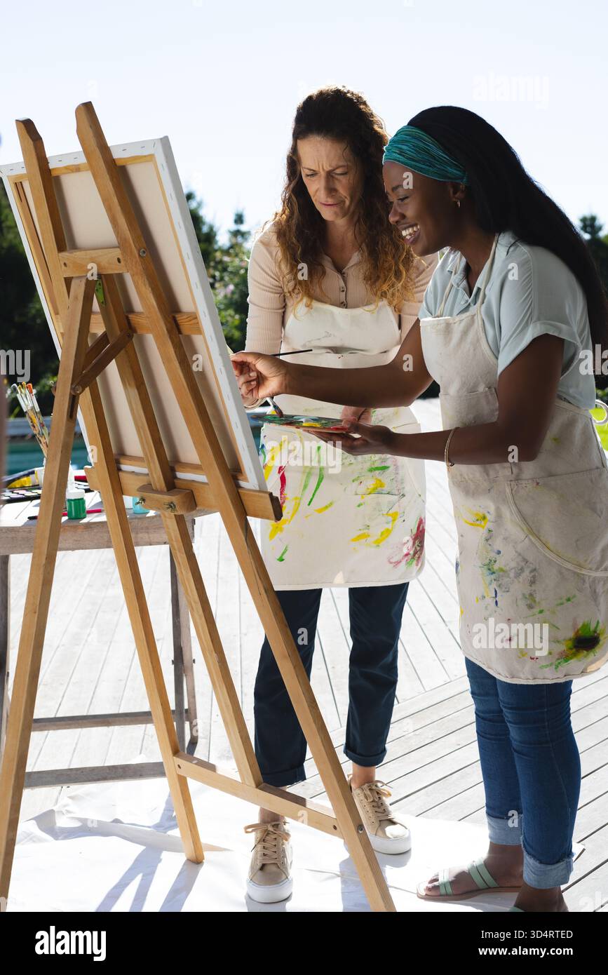 Dipingere diverse istruttrice d'arte femminile e studentessa che collabora al cavalletto sul ponte, con grembiuli Foto Stock