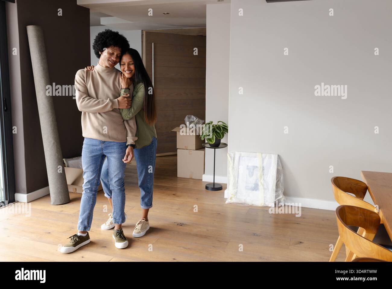 Abbracciare diverse coppie che celebrano la nuova casa in salotto, con scatole mobili e opere d'arte avvolte Foto Stock