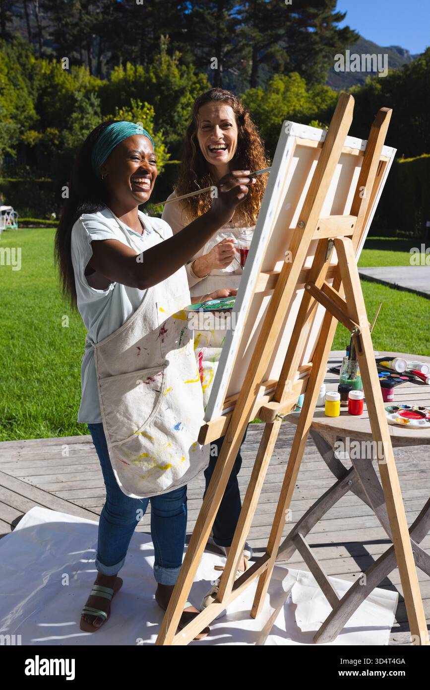 Dipingendo diverse amiche che ridono mentre dipingono sul ponte in cortile con cavalletto, vasi di pittura Foto Stock