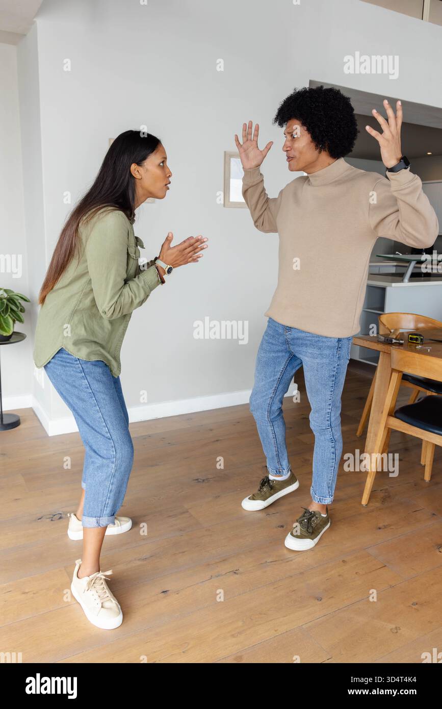 Discutere di coppie diverse in piedi l'una di fronte all'altra nella casa moderna, con lo smartphone sul tavolo da pranzo Foto Stock