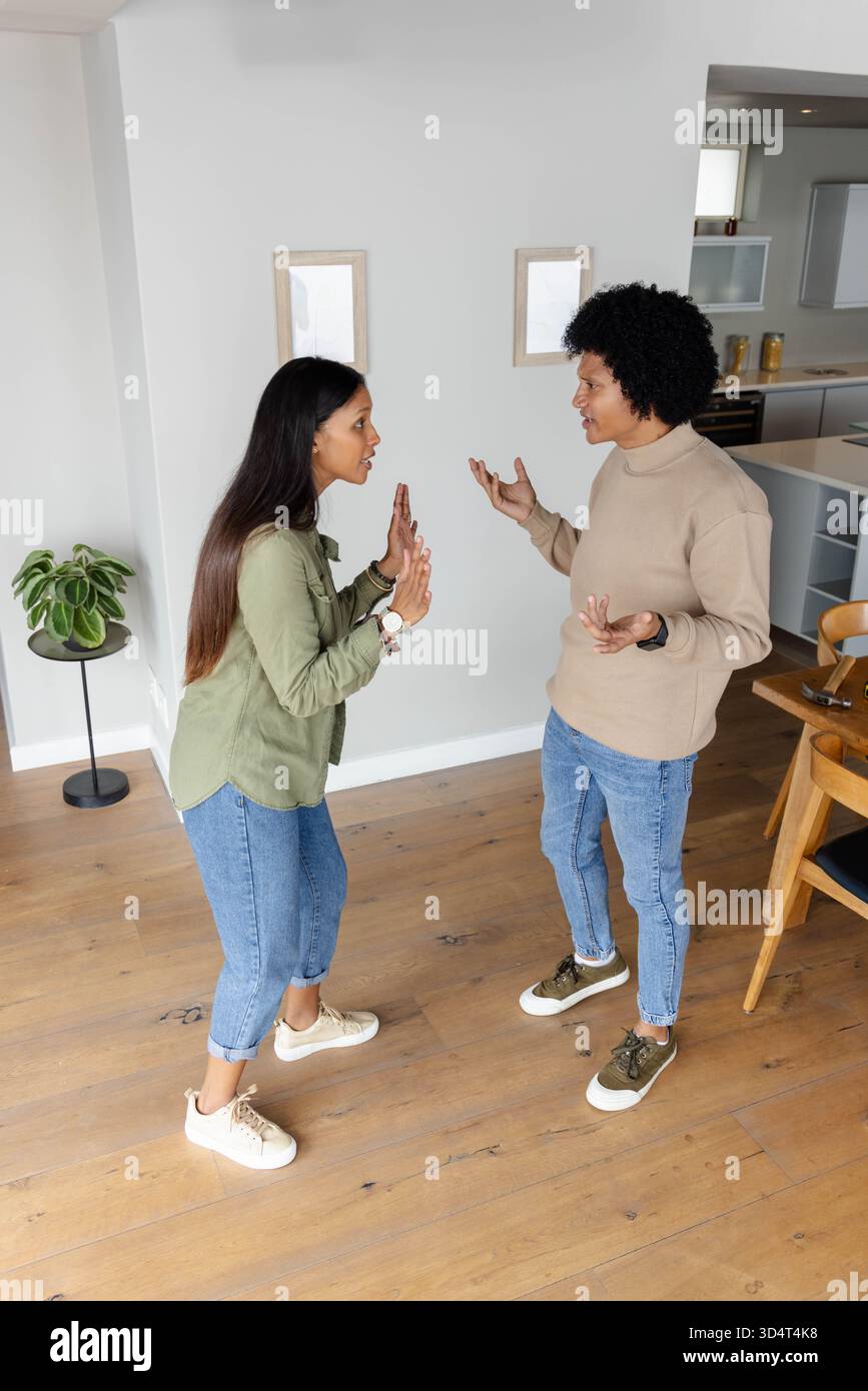Una coppia indiana parlante che ha avuto una discussione animata a casa con piante in vaso e cornici Foto Stock