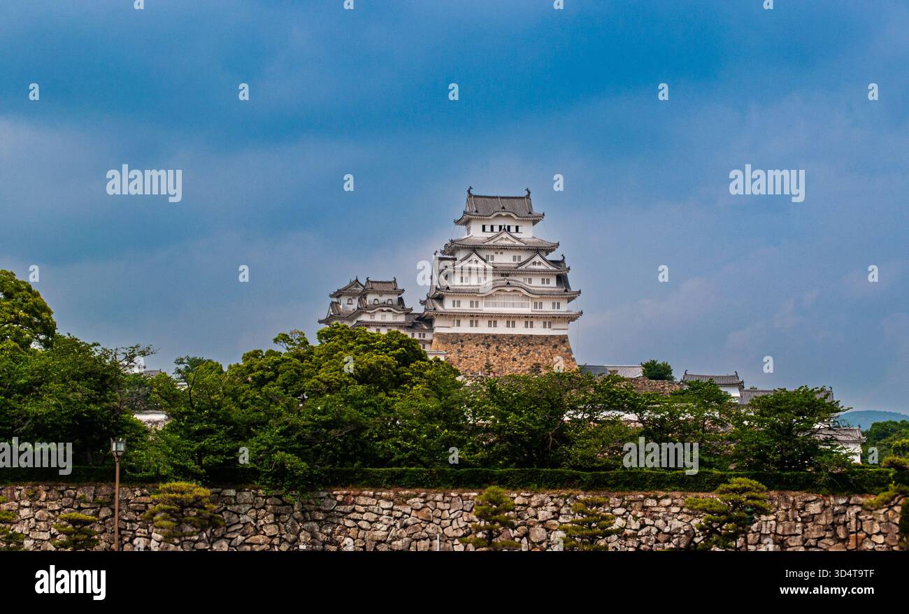 Il castello di Himeji sorge sopra una vegetazione lussureggiante sotto un cielo spettacolare. Foto Stock