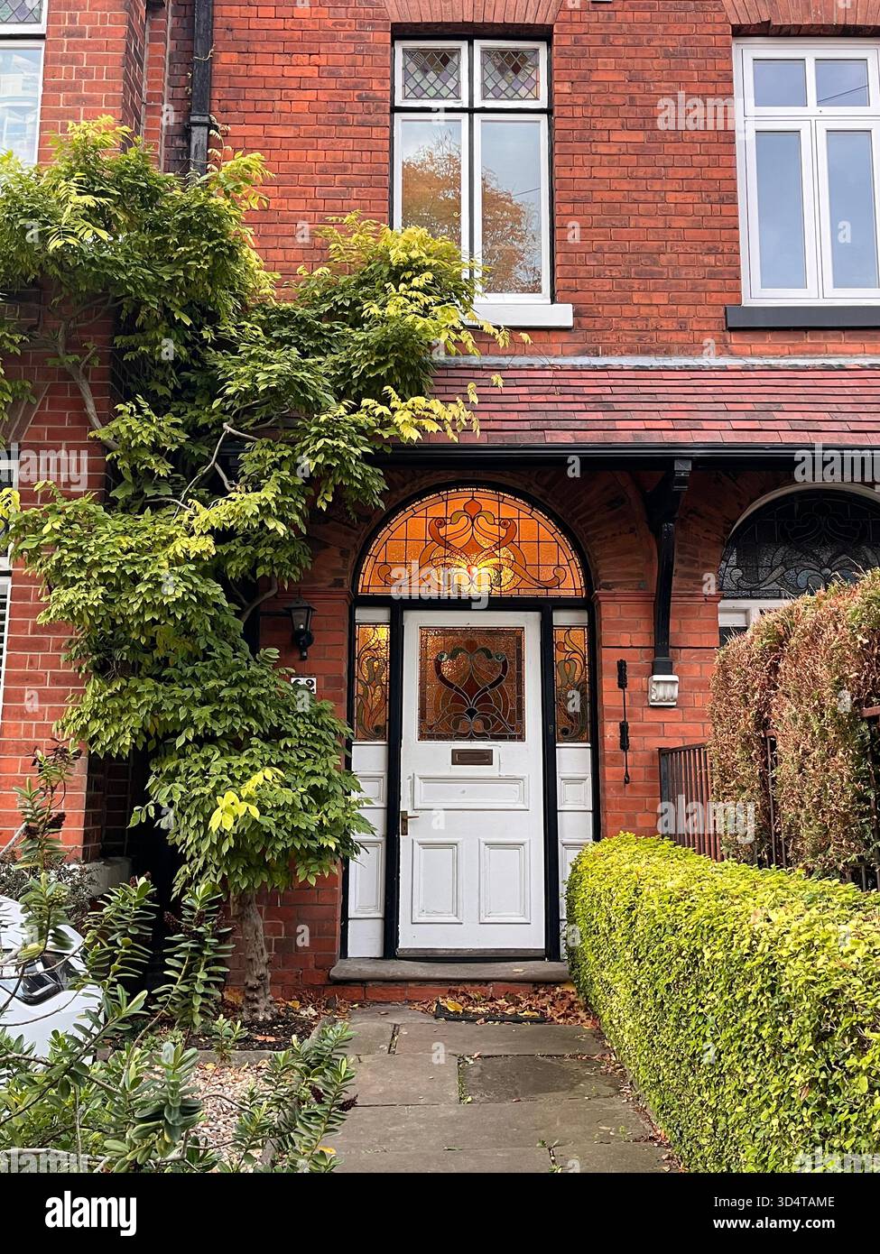 Un'affascinante casa in mattoni rossi in stile vittoriano ricoperta di edera verde, caratterizzata da una porta in vetro colorato splendidamente realizzata. Catturato a Hull, nell'East Yorkshire - Immagine stock catturata con smartphone