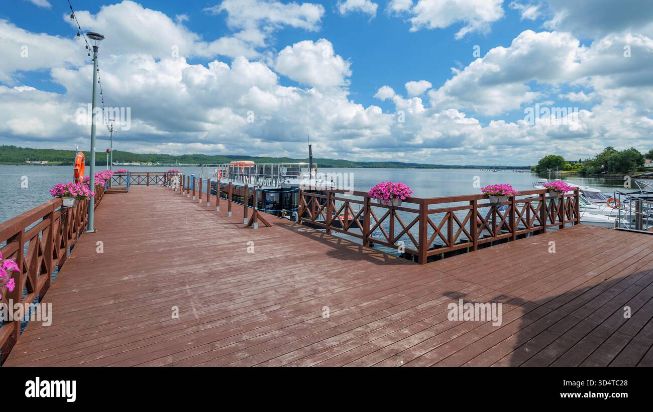 Un molo di legno sul lago Żarnowieckie. Le surfinias rosa sono appese alla ringhiera. Una bella giornata d'estate. Nadole, Kashubia, Polonia Foto Stock