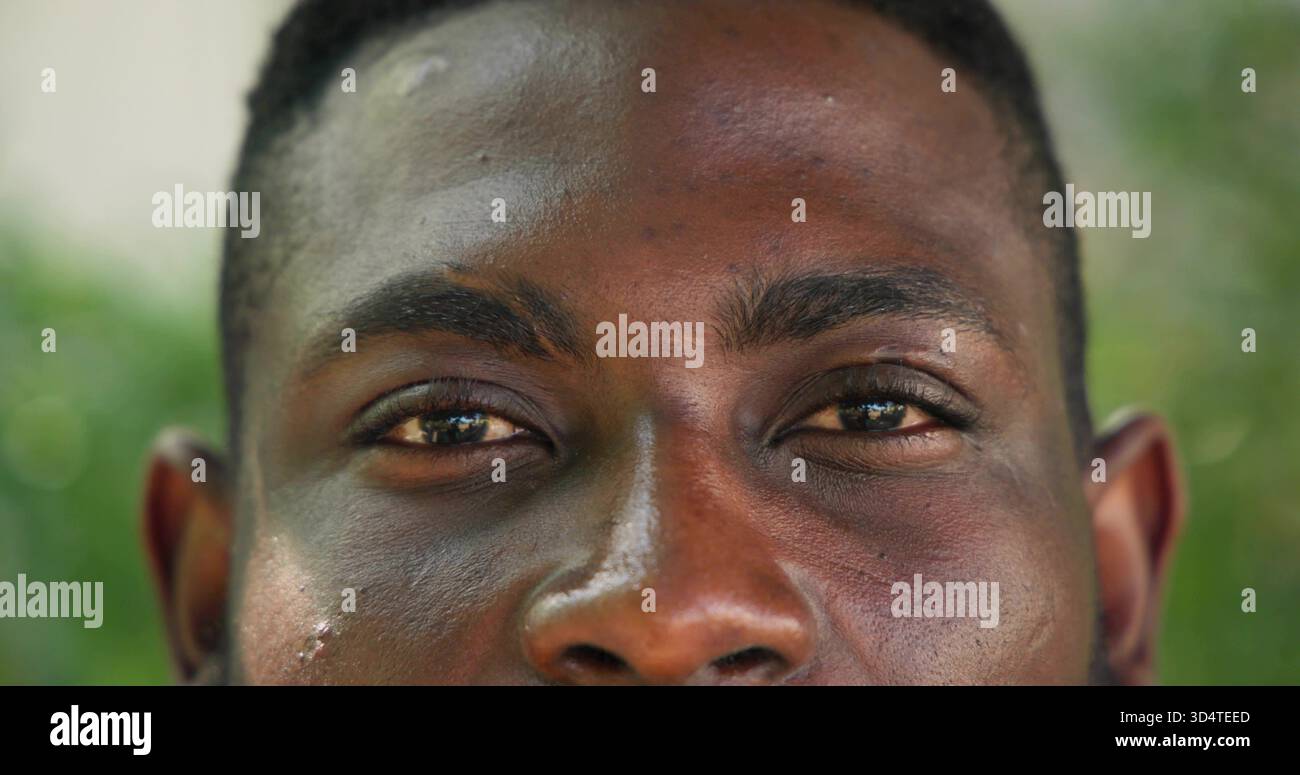 Osservando l'uomo afroamericano che riempie la cornice all'aperto, mostrando la consistenza della pelle e il bokeh verde Foto Stock