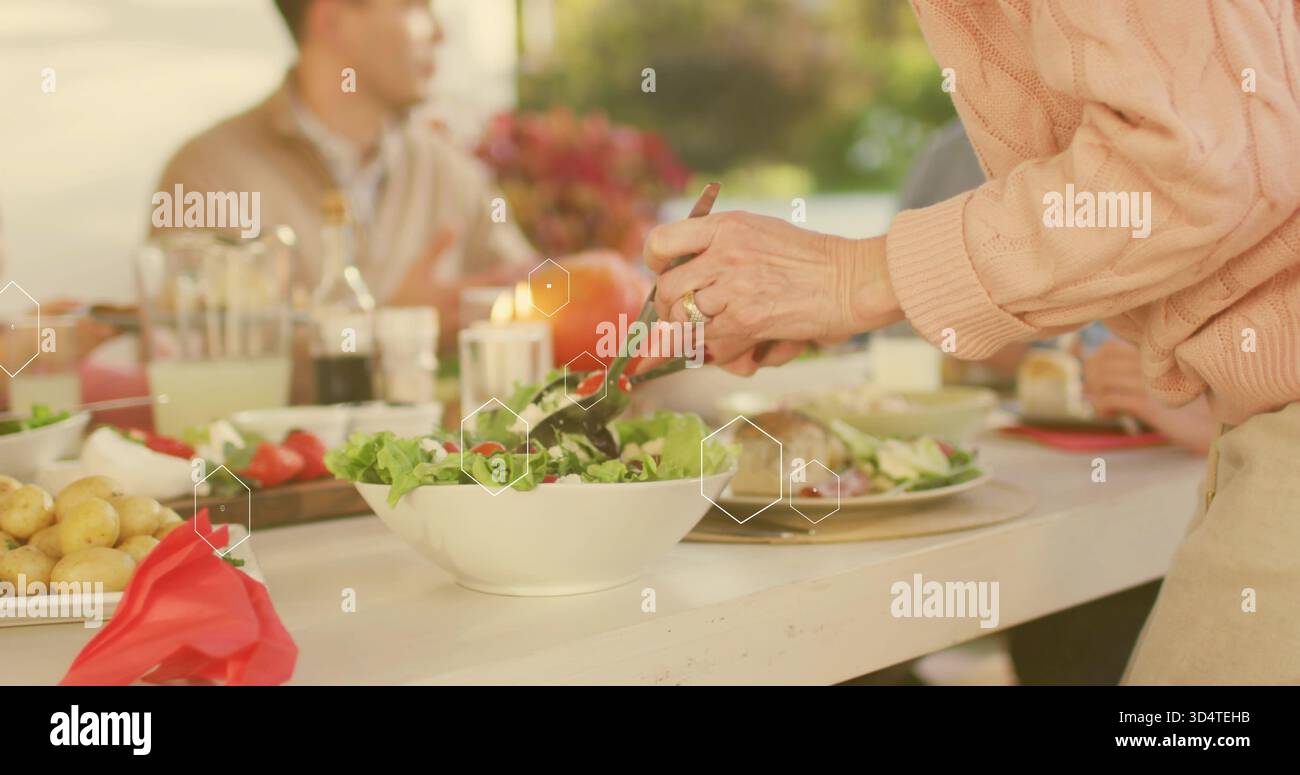 Far passare un adulto in un maglione rosa a maglia a cavo utilizzando le pinze e servire l'insalata dalla ciotola bianca al tavolo del cortile Foto Stock