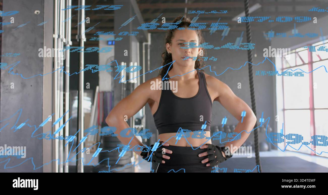 Atleta in piedi che mette le mani sui fianchi in palestra, con abbigliamento sportivo nero, attrezzatura e corde, sovrapposizioni di dati Foto Stock