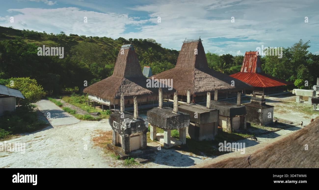 Antiche tombe megalitiche e case tradizionali con tetti di paglia testimoniano il ricco patrimonio culturale dell'isola di Sumba. Indonesia. Creare una scena accattivante sotto il cielo azzurro Foto Stock