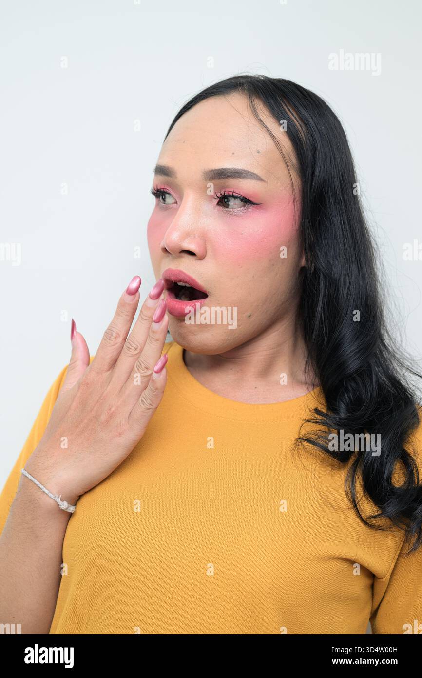 Ritratto in studio di un giovane individuo transgender thailandese con trucco e capelli lunghi. Concetto di espressione di genere, orgoglio LGBTQ e inclusività che mostra un Foto Stock