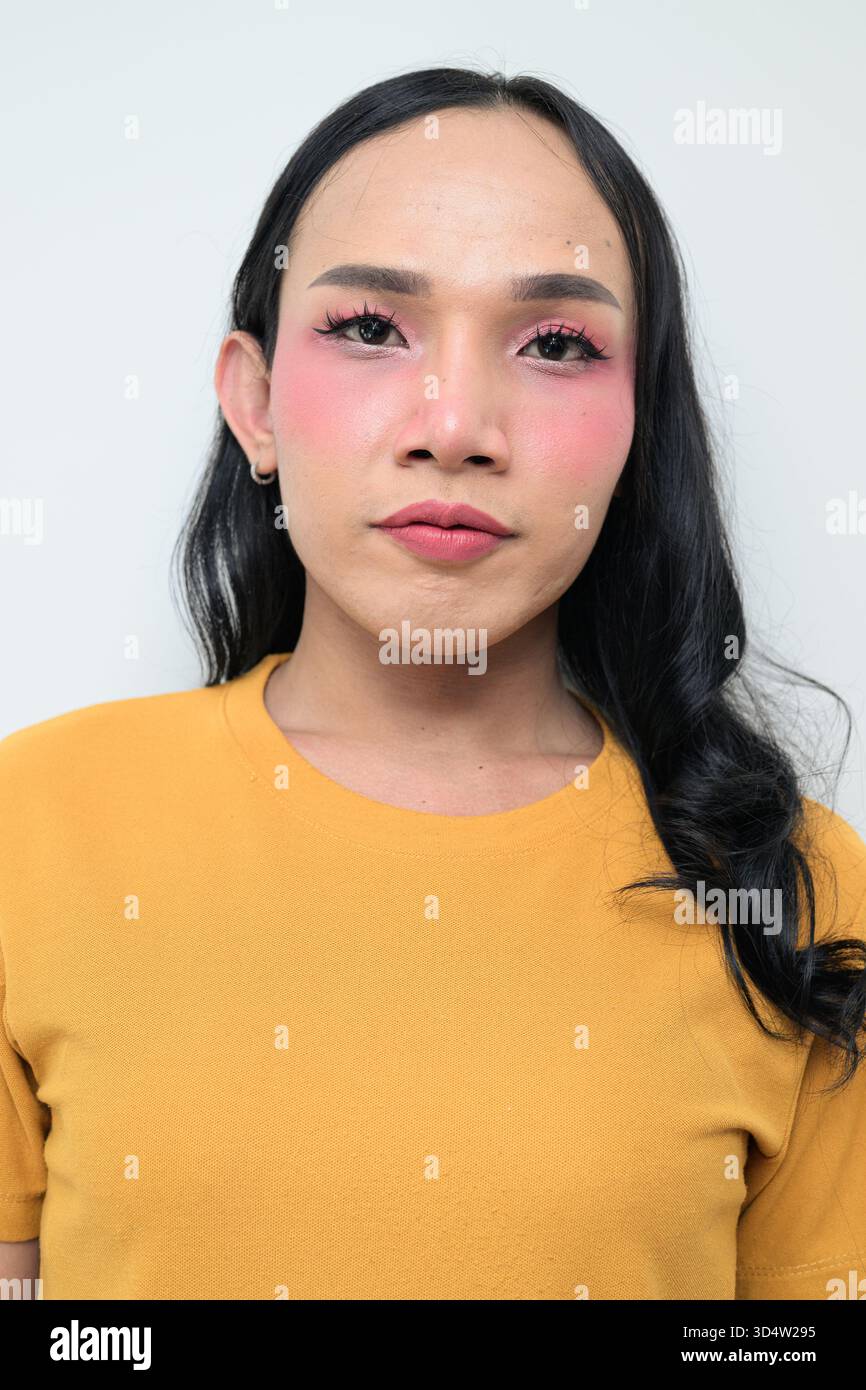 Ritratto in studio di un giovane individuo transgender thailandese con trucco e capelli lunghi. Concetto di espressione di genere, orgoglio LGBTQ e inclusività che mostra un Foto Stock
