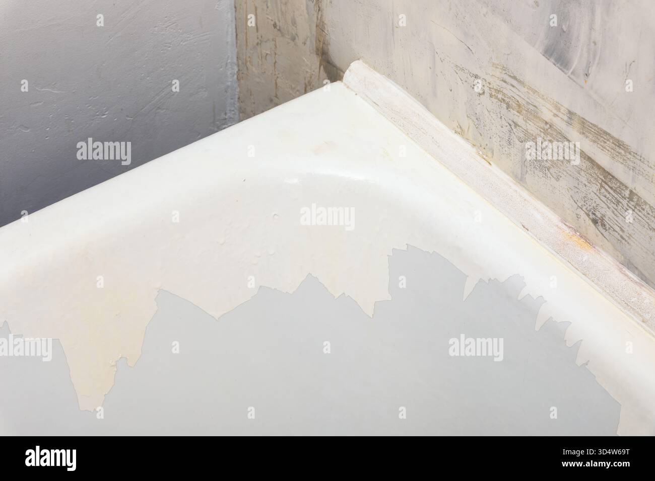 Primo piano di una vasca da bagno con vernice bianca sbucciata contro pareti non rifinite e ruvide. Ideale per progetti di ristrutturazione, riparazione o miglioramento della casa. Foto Stock