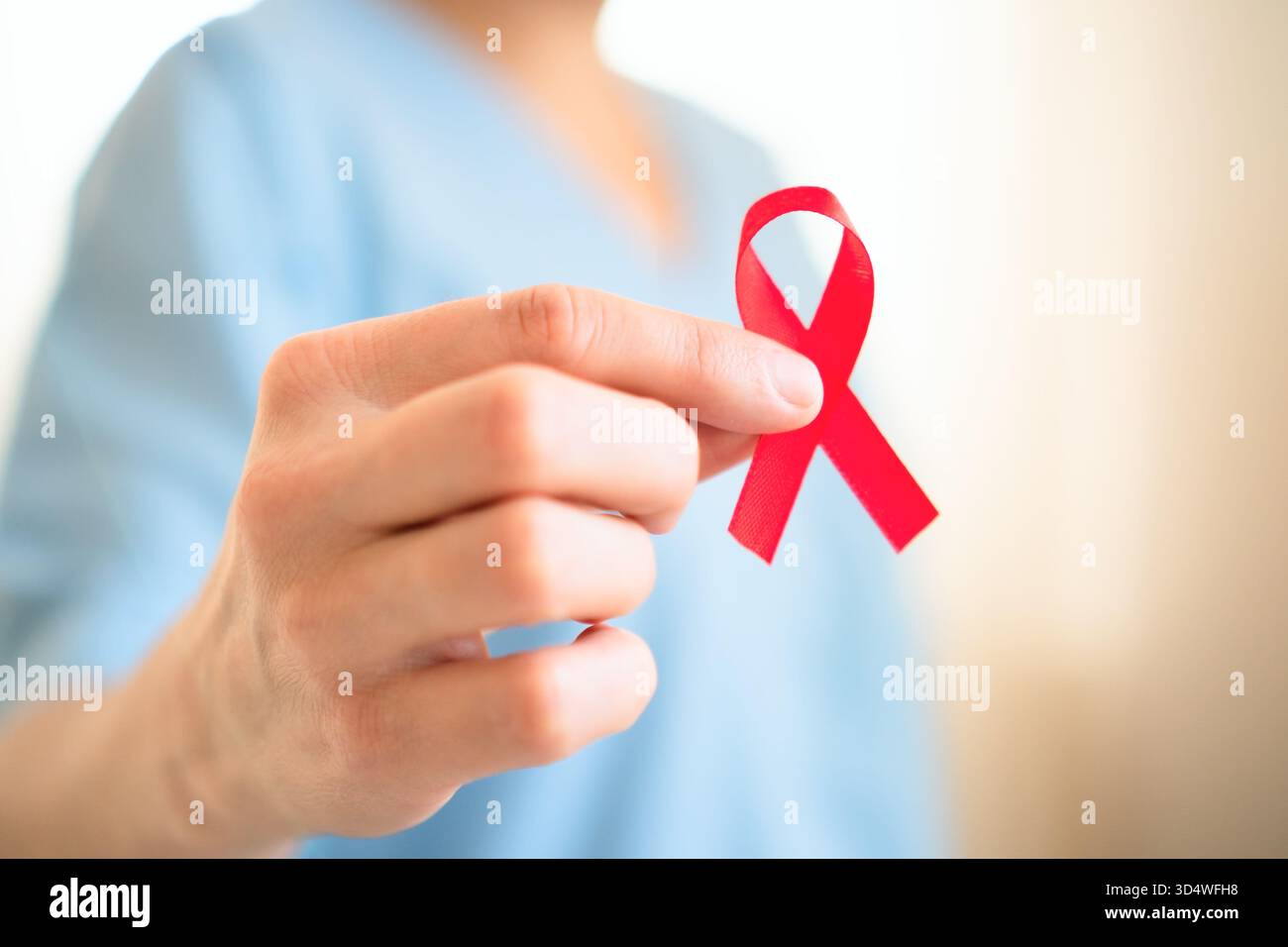 Primo piano estremo della mano femminile che tiene il nastro rosso di sensibilizzazione al raso, simboleggia la solidarietà con l'HIV AIDS, il sostegno e la speranza per le cure future. Foto Stock