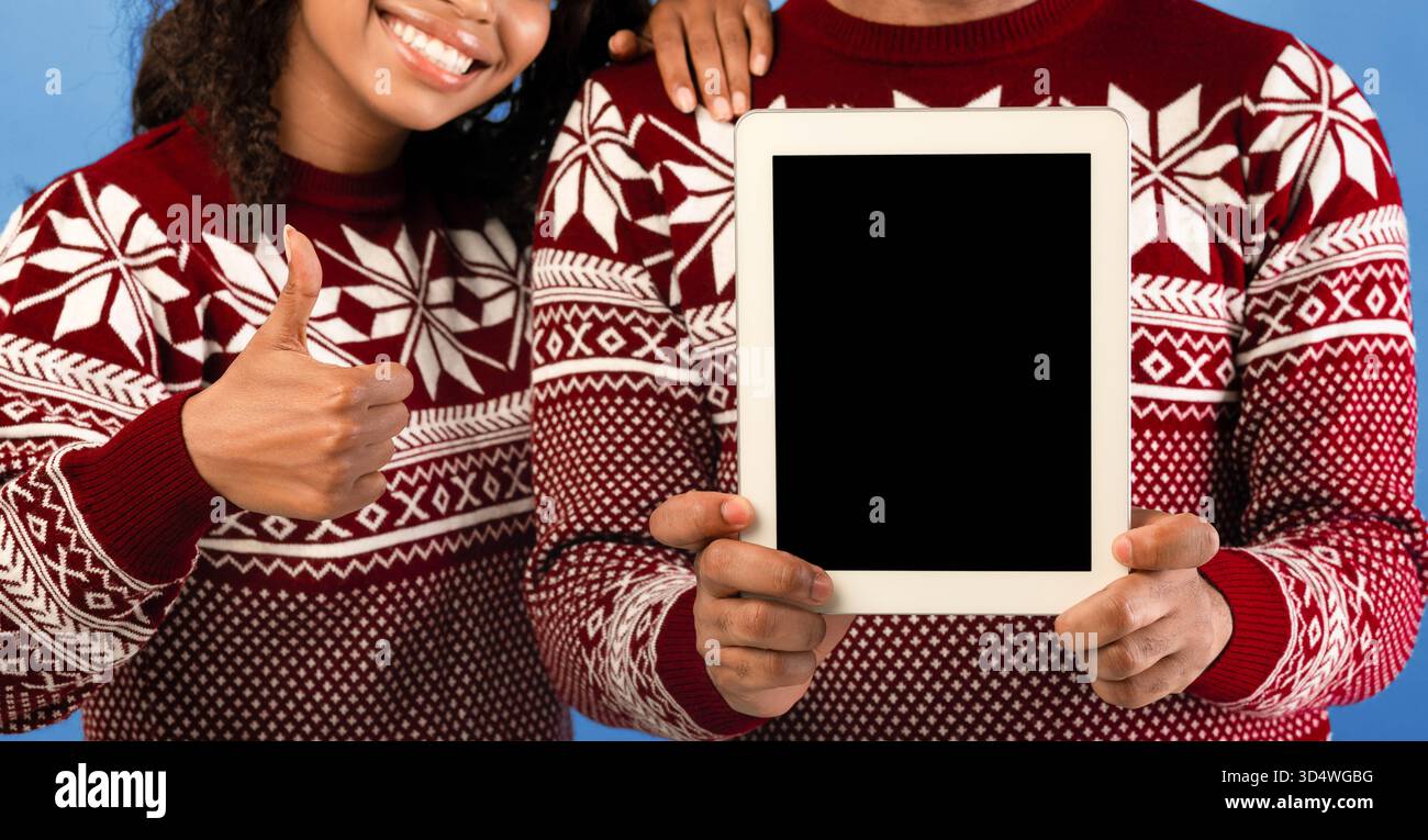 Concetto di vendite di Natale. Uomo nero che tiene il tablet con schermo vuoto e donna che mostra il pollice su sfondo blu Foto Stock