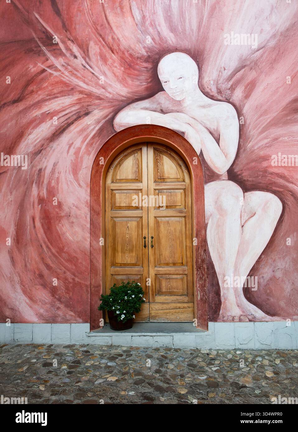 Murale artistico caratterizzato da una figura umana astratta che circonda la porta ad arco in legno che crea armonia visiva e bellezza architettonica. Foto Stock