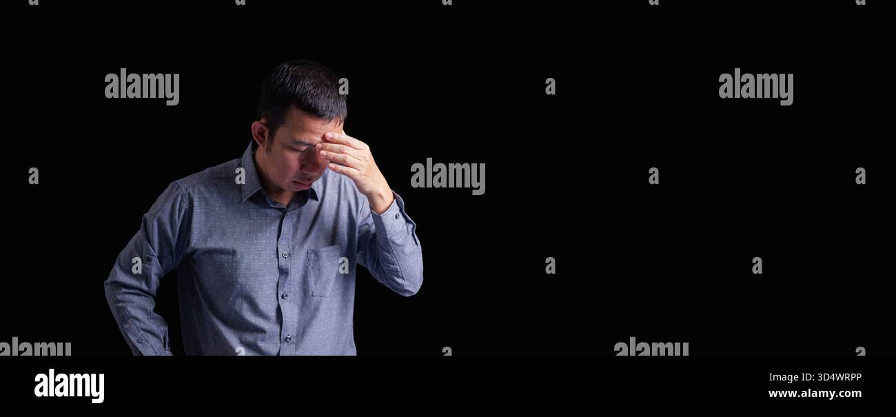 Un uomo adulto preoccupato che tocca la fronte su uno sfondo scuro, esprimendo stress, ansia e stanchezza, rappresentando la crisi finanziaria, mentale Foto Stock