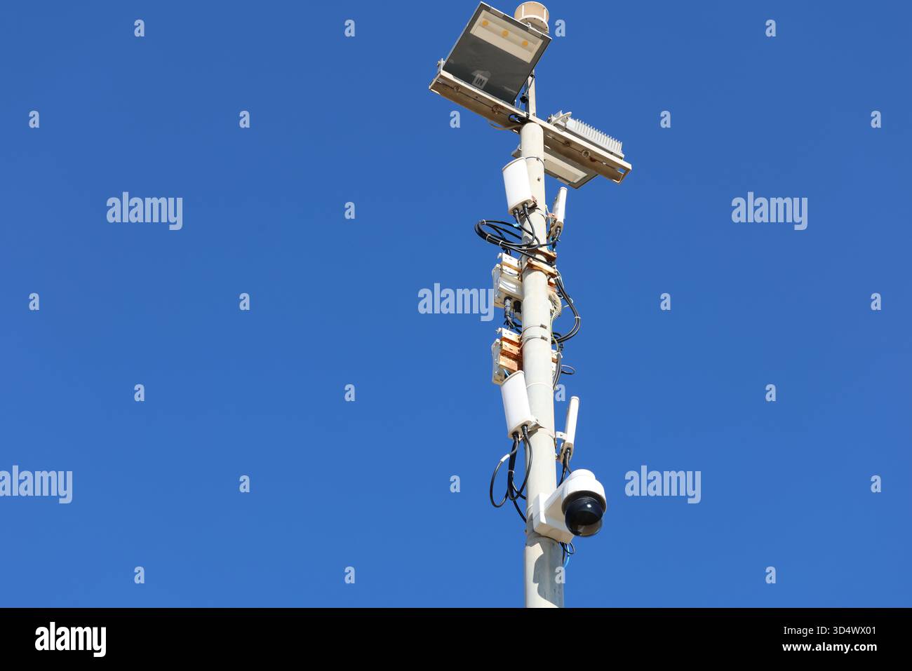 Telecamera di sorveglianza e apparecchiature di sicurezza montate su un'asta metallica alta contro un cielo azzurro, utilizzate per il monitoraggio e la pubblica sicurezza Foto Stock
