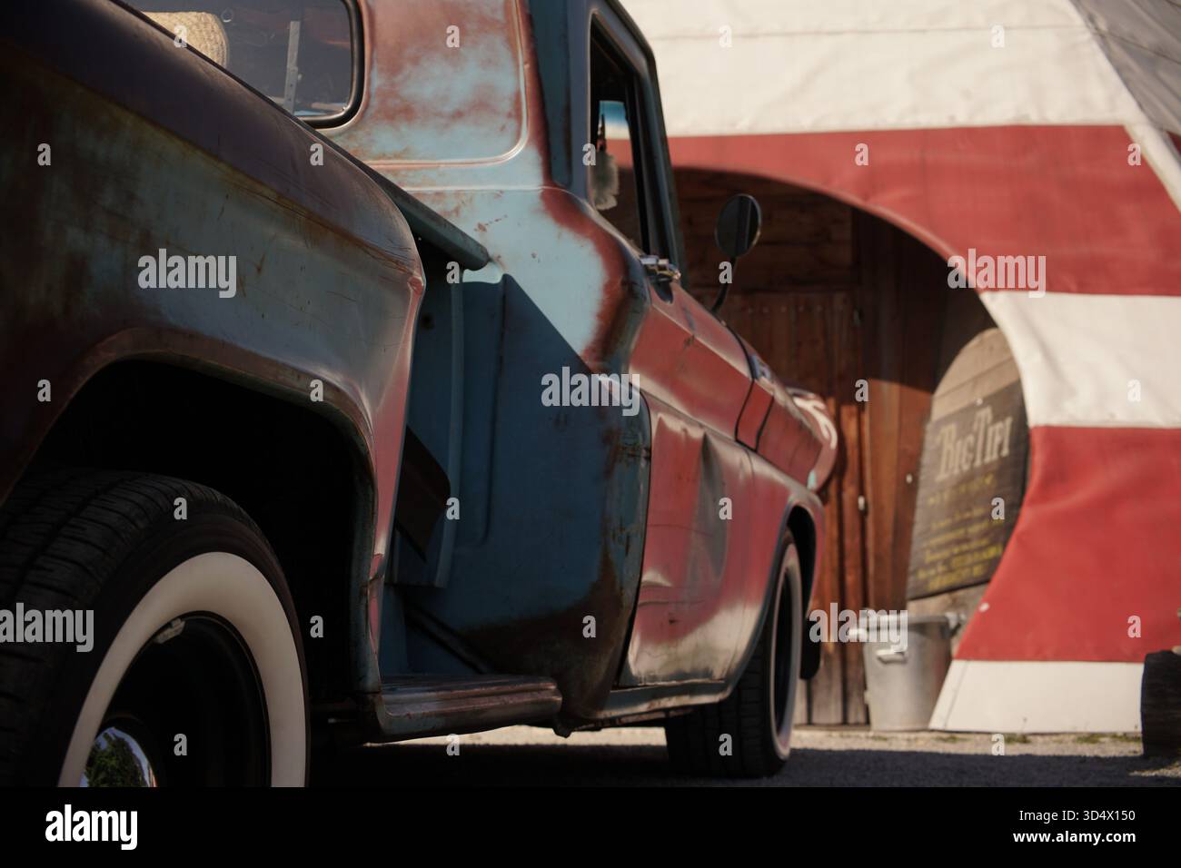 Rustico pick-up vintage parcheggiato accanto a una struttura simile a una tenda in un luogo all'aperto, che mostra vernice resistente agli agenti atmosferici, patina e stile retrò. Foto Stock