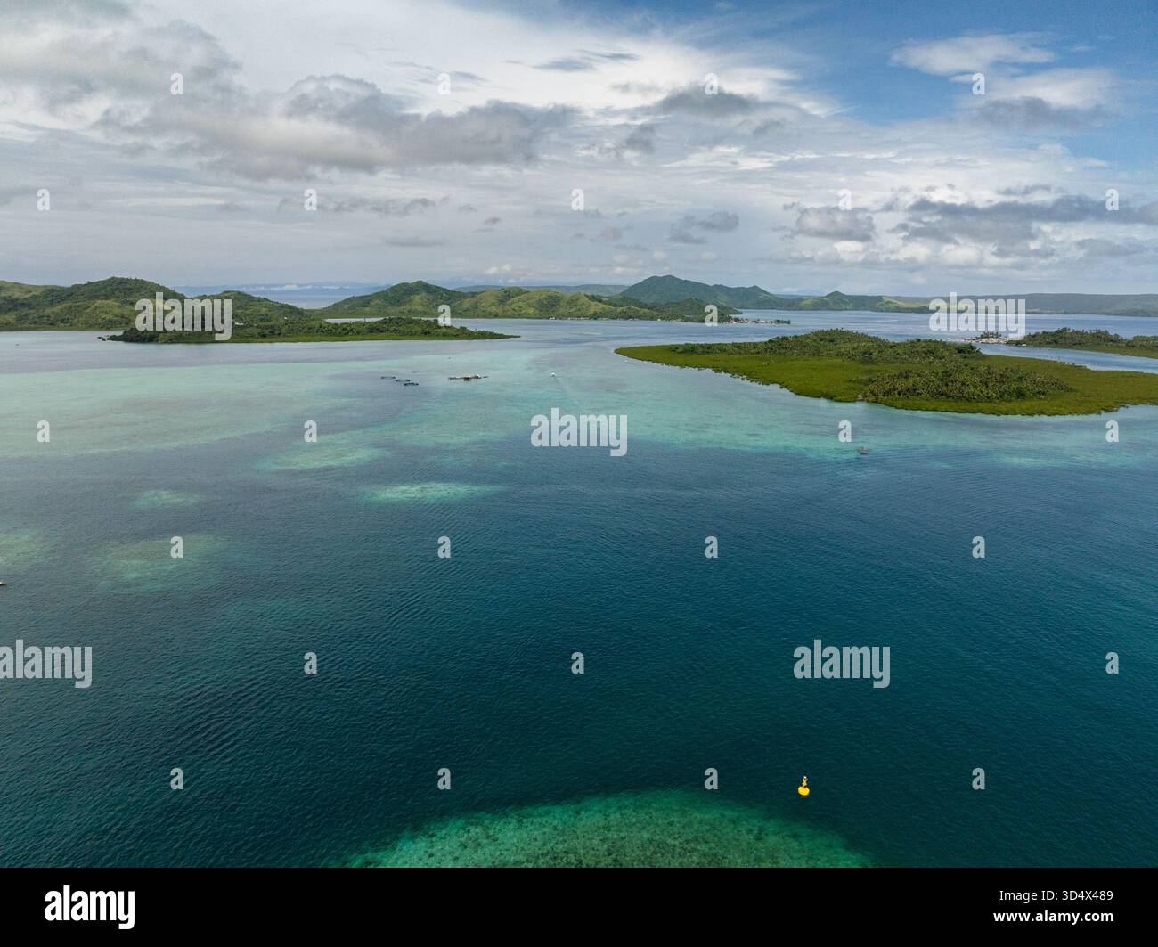 Lussureggianti isole verdi circondate da acque turchesi poco profonde e coralli macchie sotto cieli parzialmente nuvolosi. Foto Stock
