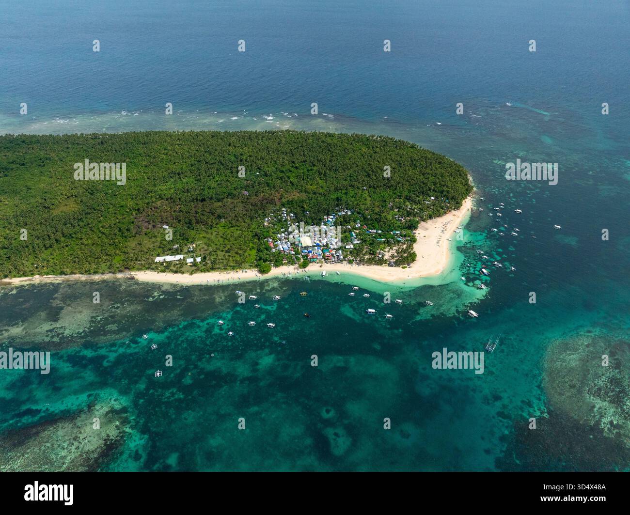 Villaggio costiero con case raggruppate circondato da foresta tropicale e barche ancorate vicino alla spiaggia. Isola di Daku. Siargao, Filippine. Foto Stock