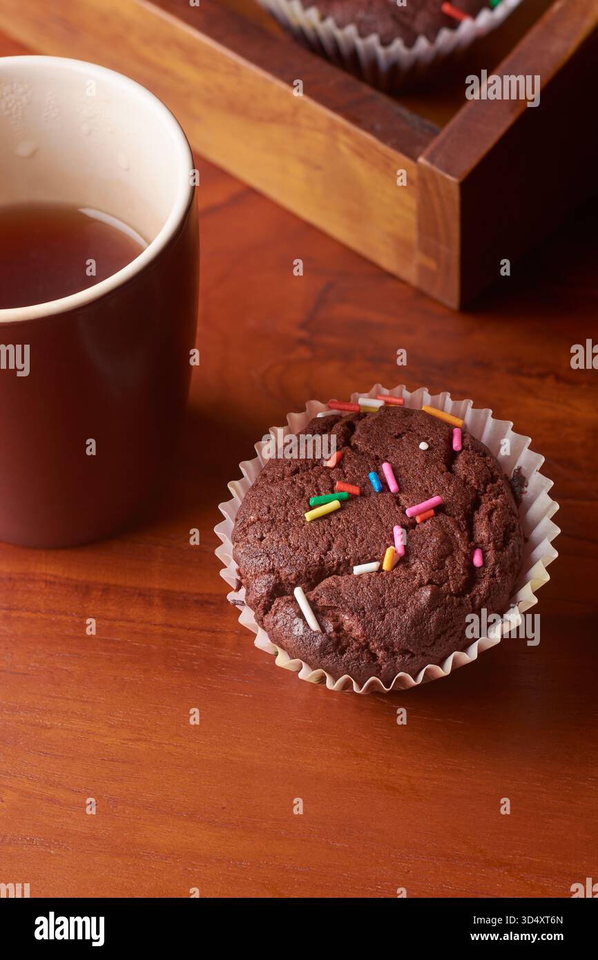 muffin al cioccolato con cospargi di caffè caldo o tè sulla superficie del tavolo in legno marrone rossastro, messa a fuoco morbida con spazio per copiare il testo, pausa confortevole Foto Stock