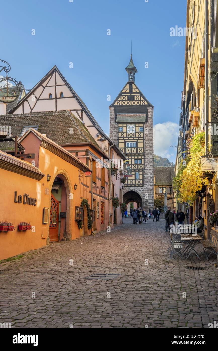 Strada principale con tradizionali case in legno e torre di guardia Dolder, Riquewihr, Haut-Rhin, Grand Est, Francia Foto Stock