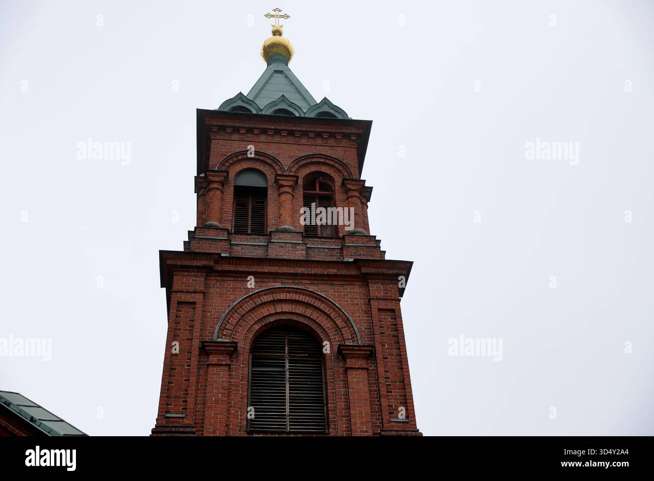 Campanile della cattedrale di Uspenski con finestre ad arco, guglia verde e croce d'oro a Helsinki, Finlandia, fotografato verso l'alto contro il cielo bianco. Foto Stock