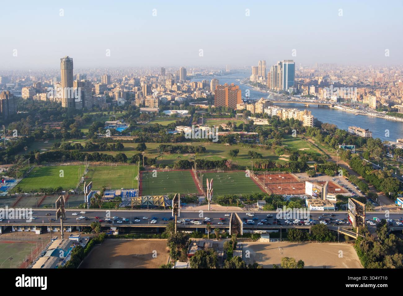Vista di vivaci spazi verdi ed edifici annidati lungo il Nilo, con una vivace autostrada sottostante, il tutto sotto un cielo nebbioso, Zamalek, il Governatorato del Cairo, ad esempio Foto Stock