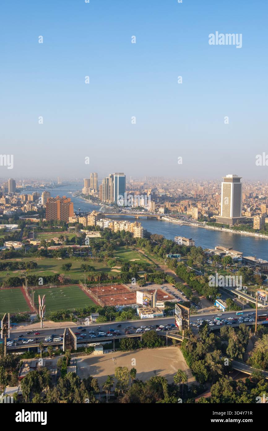 Vista del fiume Nilo che serpeggia attraverso un vibrante paesaggio urbano, edifici moderni che si innalzano in alto contro lo skyline, lussureggiante vegetazione e strade trafficate sottostanti, Zamale Foto Stock