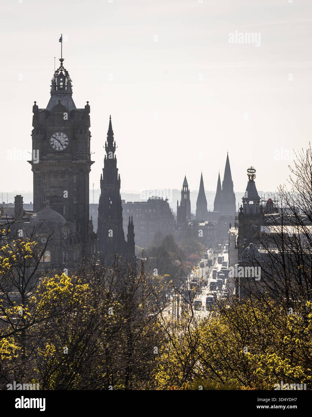 La vista della torre dell'orologio Balmoral e delle guglie gotiche punteggiano lo skyline sopra una vivace strada incorniciata dal fogliame primaverile, Edimburgo, Scozia, United Foto Stock