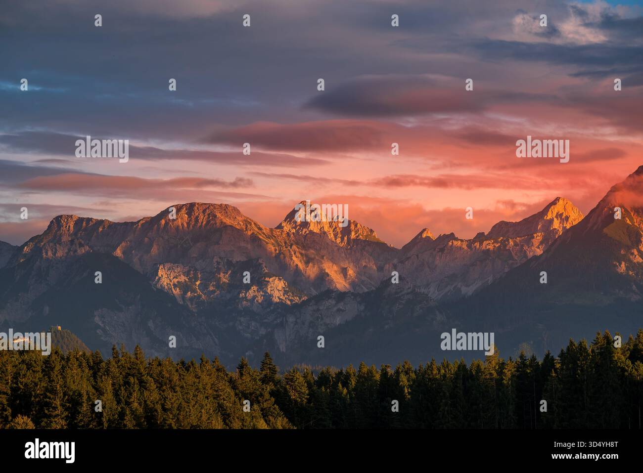 Vista delle maestose vette delle montagne baciate da un vibrante tramonto, che proietta una calda luce sulla lussureggiante foresta verde sottostante, Nesselwang, Bayern, Germania. Foto Stock