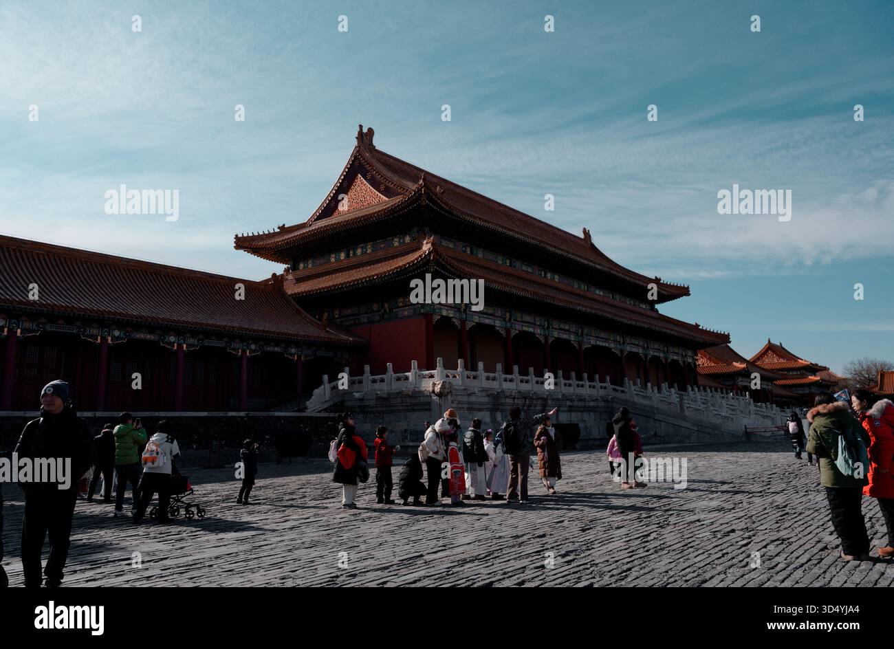 All'interno della città Proibita, i visitatori si trovano su un cortile acciottolato illuminato dal sole, sotto il palazzo ornato, in un pomeriggio d'inverno Foto Stock
