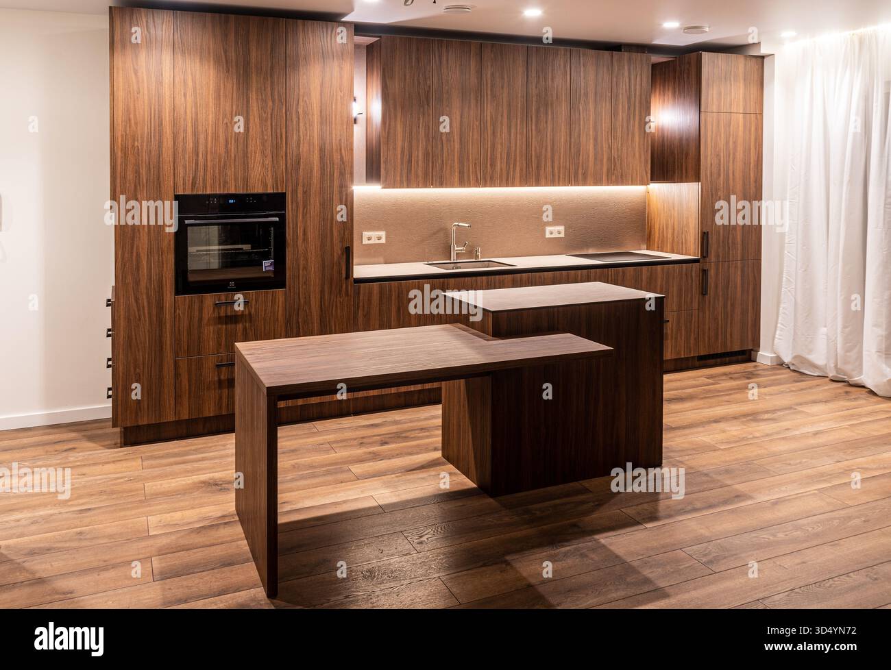 Gli interni moderni della cucina sono dotati di armadi in legno, elettrodomestici integrati e una calda illuminazione ambiente che mette in risalto un design minimalista Foto Stock