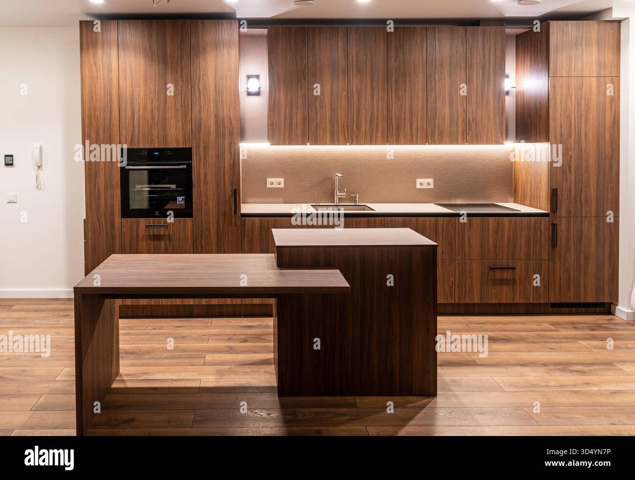 Gli interni moderni della cucina sono dotati di armadi in legno, elettrodomestici integrati e una calda illuminazione ambiente che mette in risalto un design minimalista Foto Stock