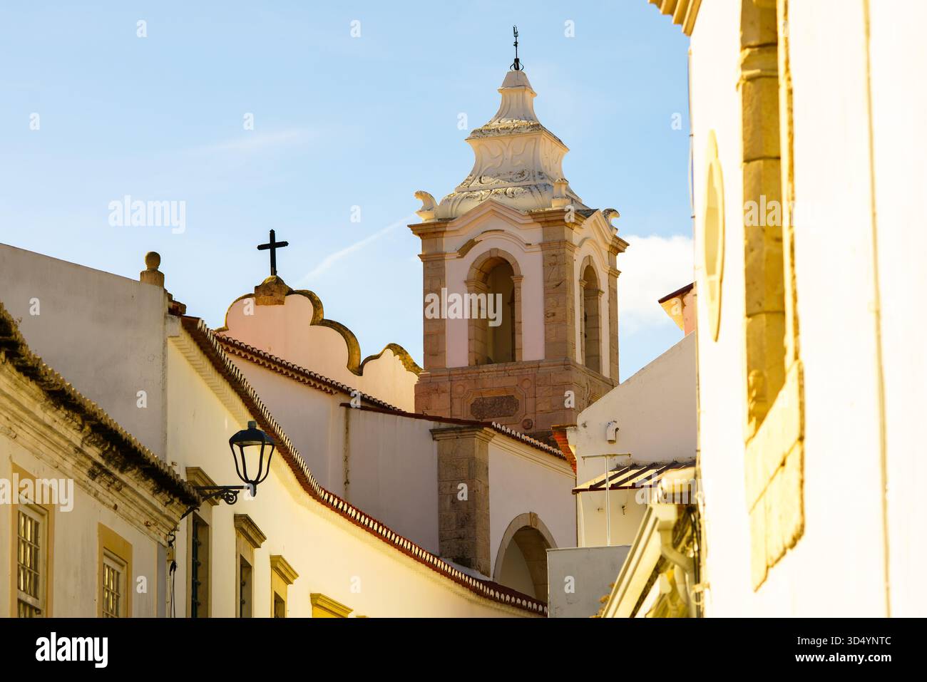 Una storica torre della chiesa con dettagli ornati si erge ben sopra edifici imbiancati sotto un cielo blu. Foto Stock