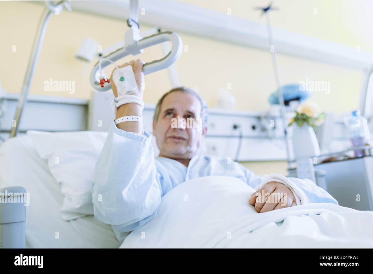 Ritratto uomo di mezza età seduto su un letto d'ospedale adattivo, che tiene il corrimano appeso per ottenere assistenza. Attrezzature di comfort per l'ospedale Foto Stock