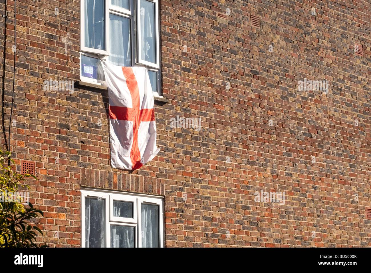 LONDRA - 6 OTTOBRE 2025: Bandiera della Croce di San Giorgio appesa da una finestra su una casa di mattoni Foto Stock