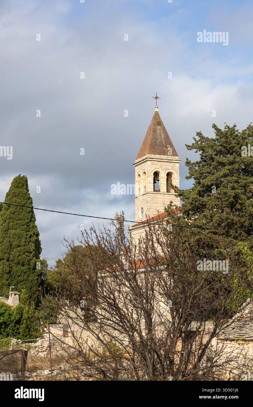 Idilliaco scenario rurale che mostra un affascinante villaggio costruito in pietra con una torre di chiesa circondata dal verde sotto un cielo azzurro. Foto Stock