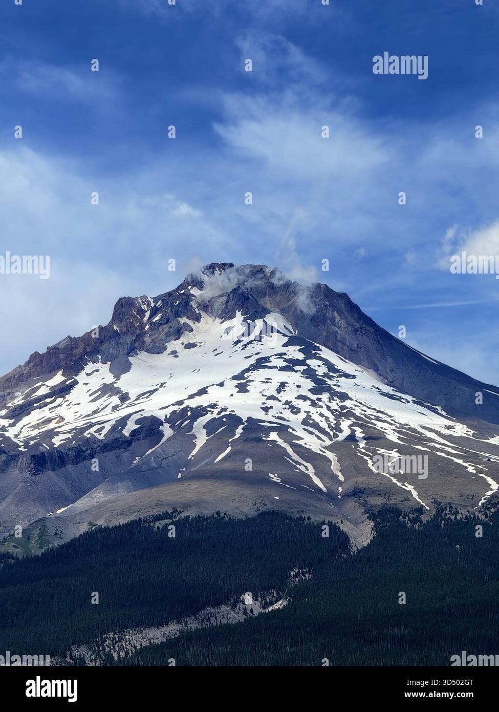 Un imponente monte Cappuccio ricoperto di neve leggera in una tarda estate, nuvole sussurranti in cima alle cime Foto Stock