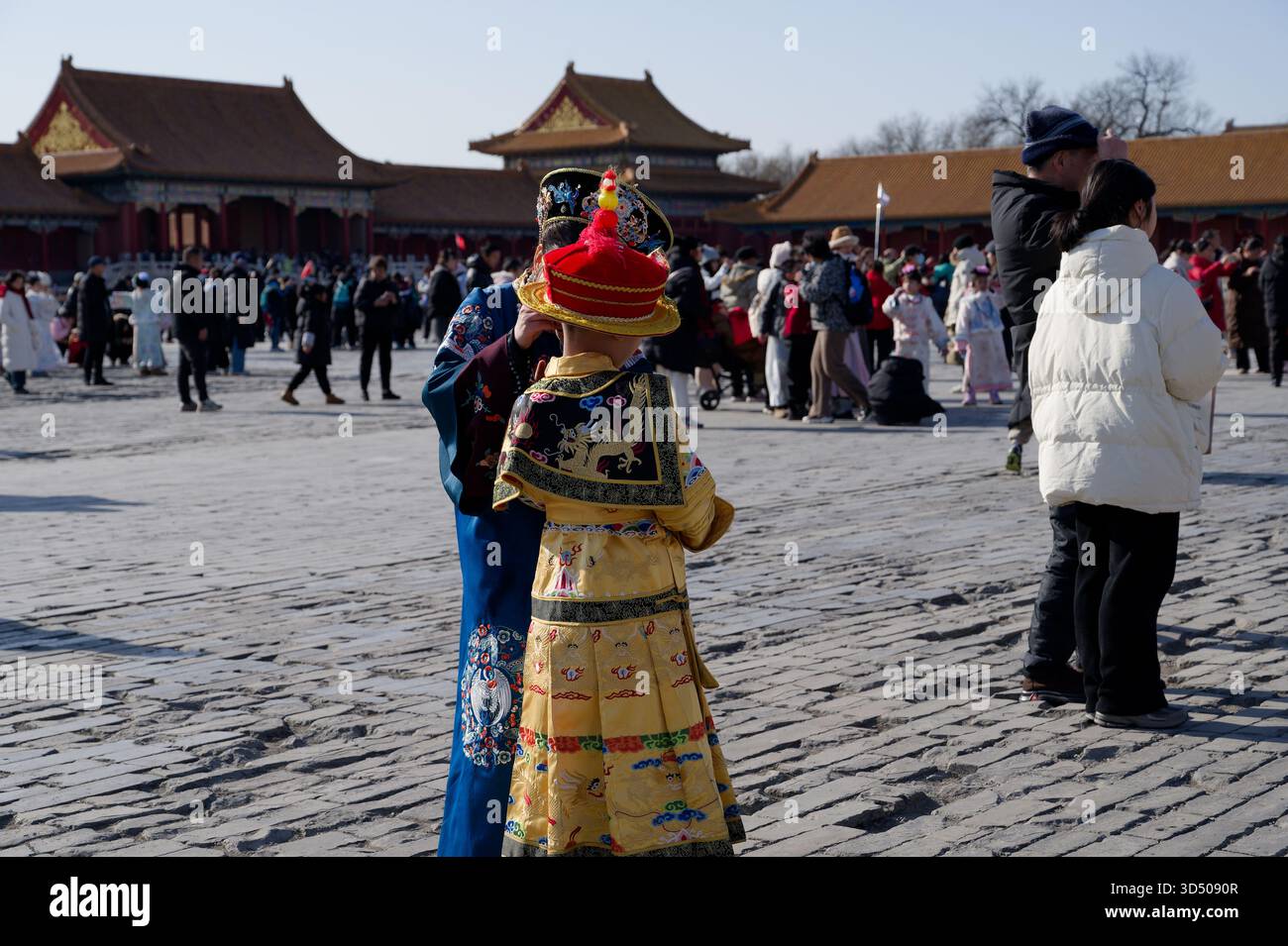 Madre adatta il costume imperiale di suo figlio nel vasto cortile della città Proibita di Pechino, tra la folla invernale Foto Stock