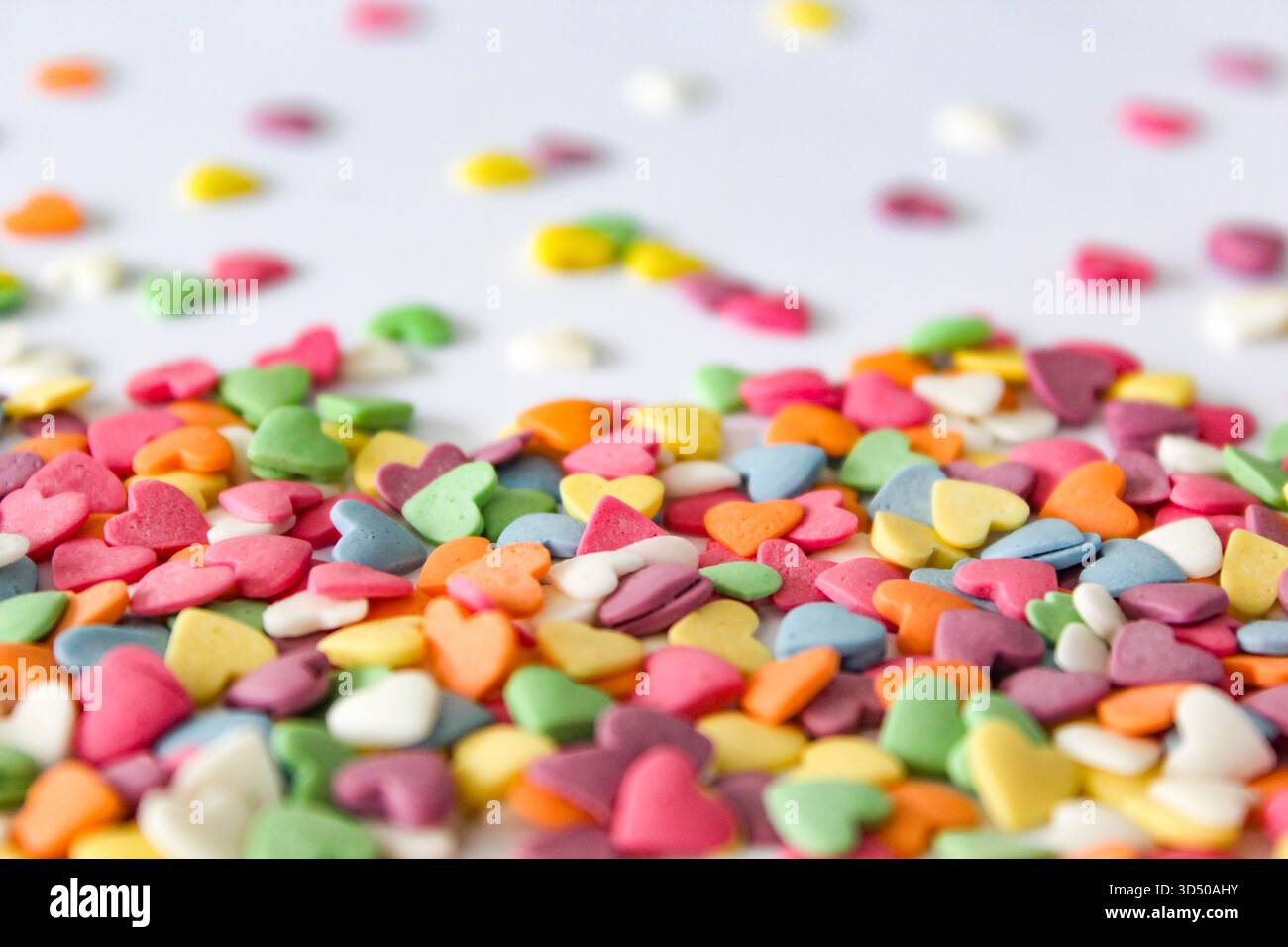 Scintillanti e colorate spruzzette a forma di cuore sono disposte su una superficie bianca, aggiungendo un tocco divertente e festoso a varie prelibatezze per festeggiare o. Foto Stock