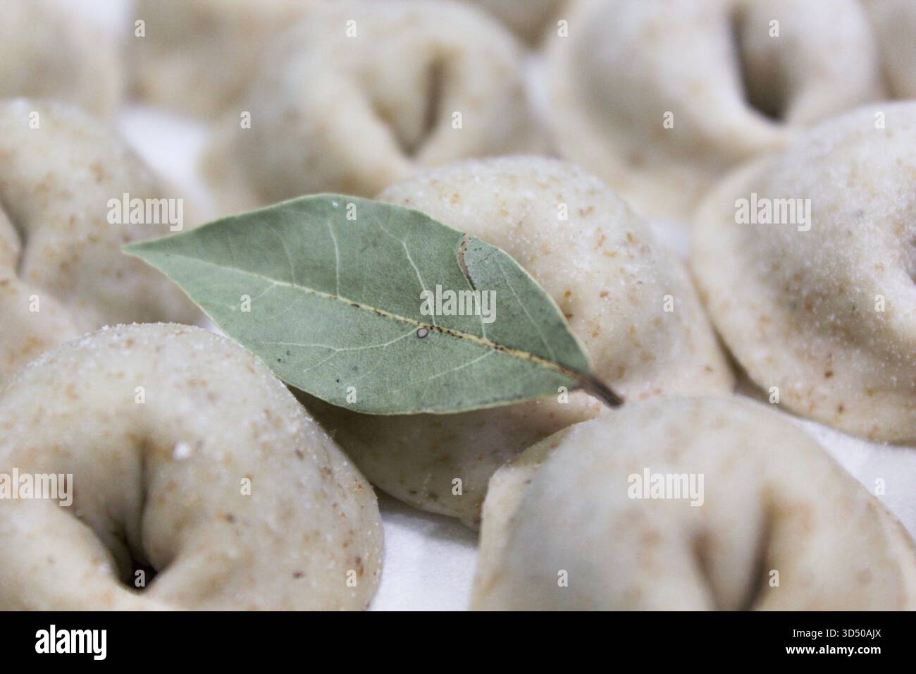 I gnocchi poggiano su una superficie, mostrando le loro forme uniche come una singola foglia di alloro aggiunge un tocco aromatico. L'atmosfera accogliente della cucina invita a un senso di benessere Foto Stock