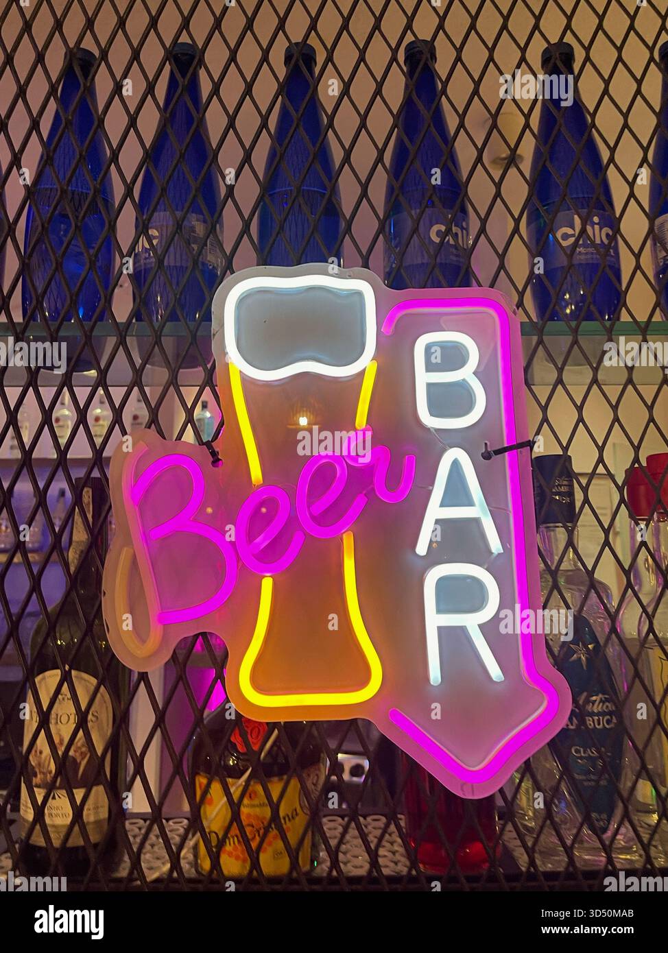 Il cartello al neon "Bar OPEN" si illumina di rosa, blu e giallo contro mesh e bottiglie, invitando gli ospiti a vivere una vivace vita notturna Foto Stock