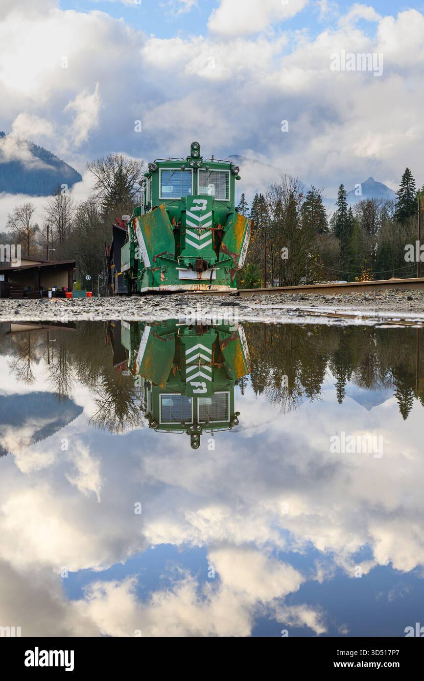 Skykomish, Washington, Stati Uniti d'America - 10 novembre 2025; attrezzatura per lo sgombero della neve a Burlington Northern che si riflette in un puddle in attesa dell'inverno Foto Stock