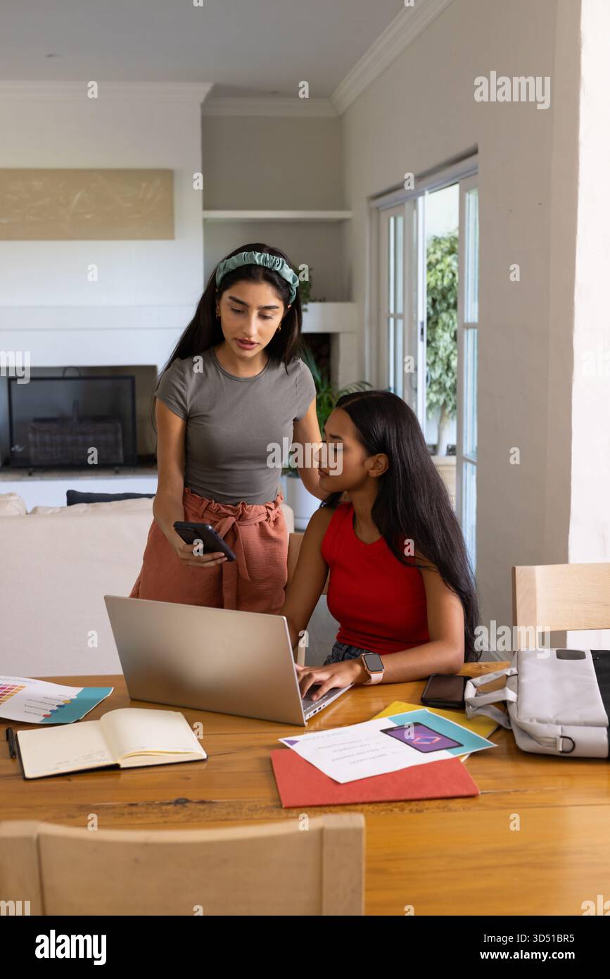 Collaborare con diverse amiche che lavorano a un tavolo da pranzo a casa, con un computer portatile e uno smartphone Foto Stock