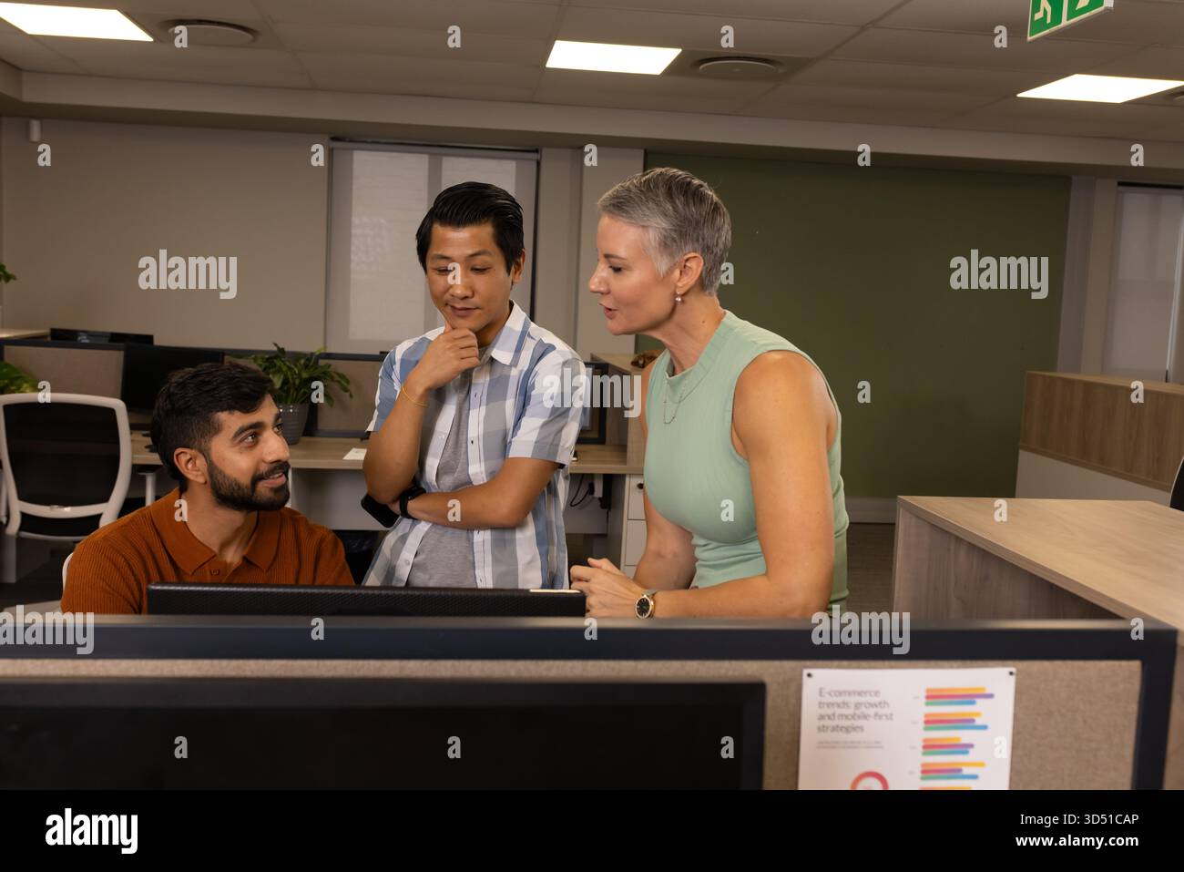 Diversi colleghi che analizzano il grafico a barre stampato in un moderno ufficio open space, con impianto in vaso Foto Stock