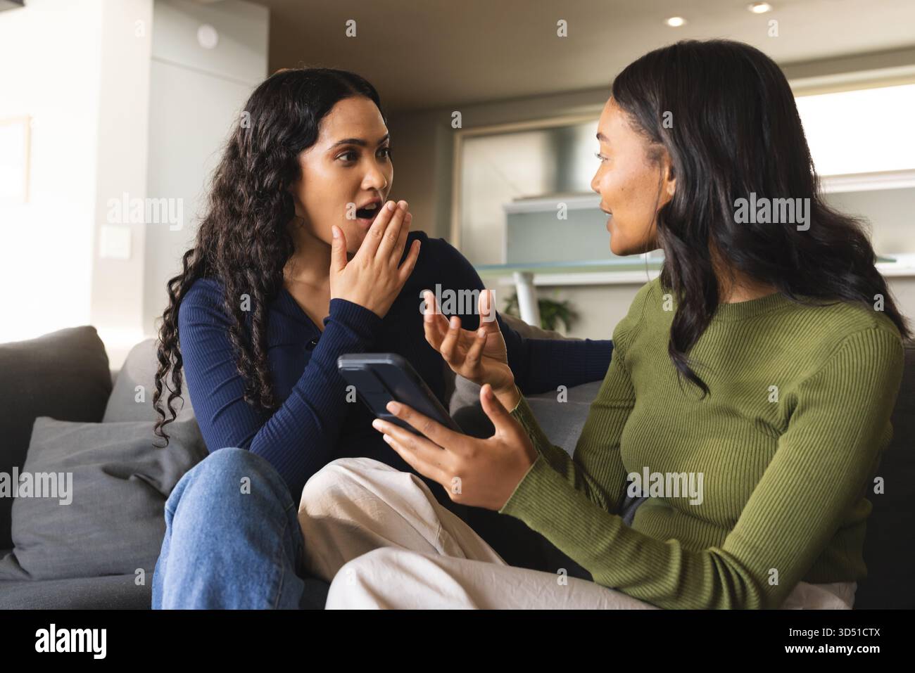 Tenendo in mano lo smartphone diverse amiche sul divano grigio nel moderno soggiorno, con cucina Foto Stock