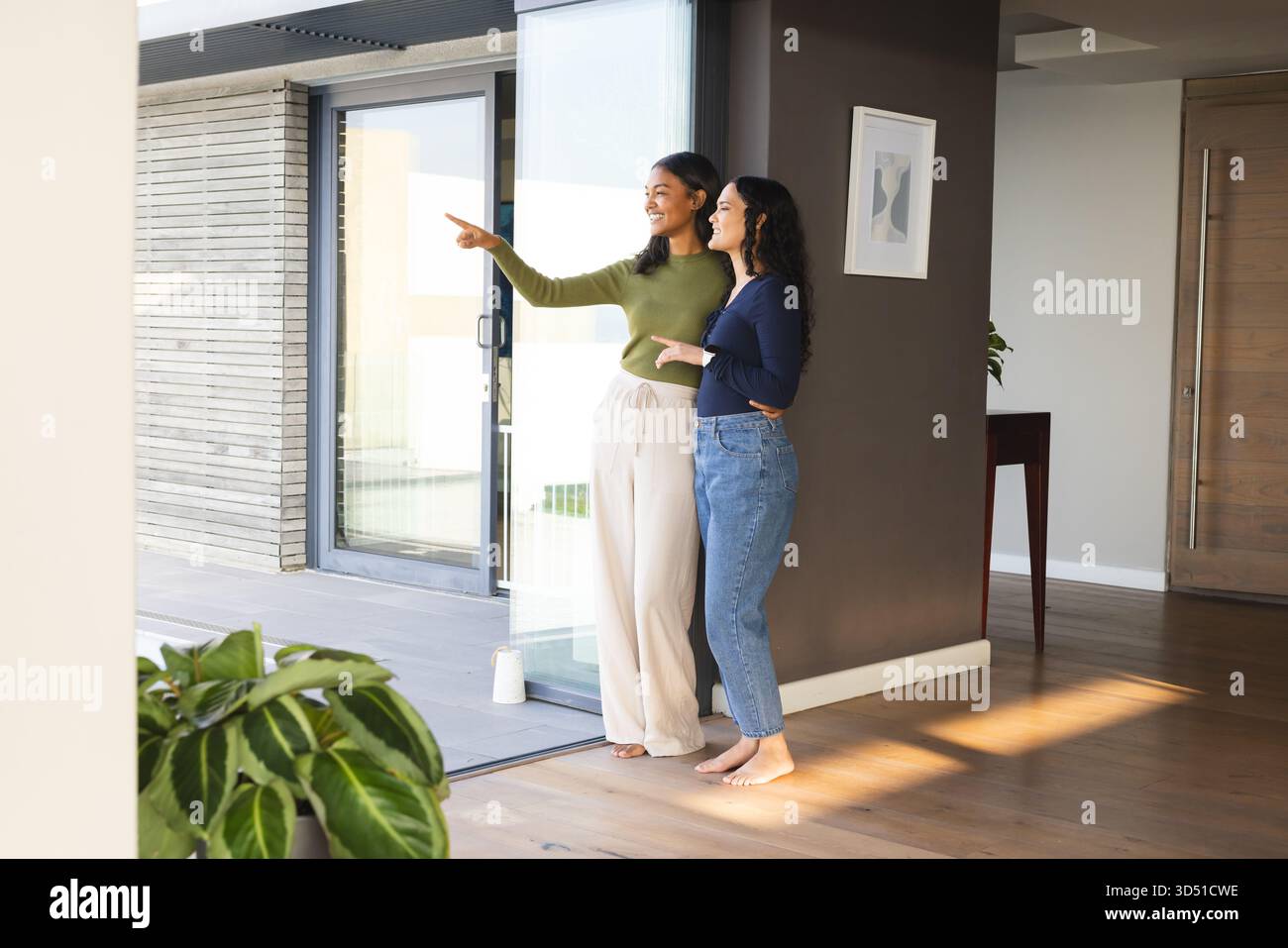 Diverse amiche che puntano al patio esterno e sorridono a casa, con porte in vetro e spazio per copiare Foto Stock
