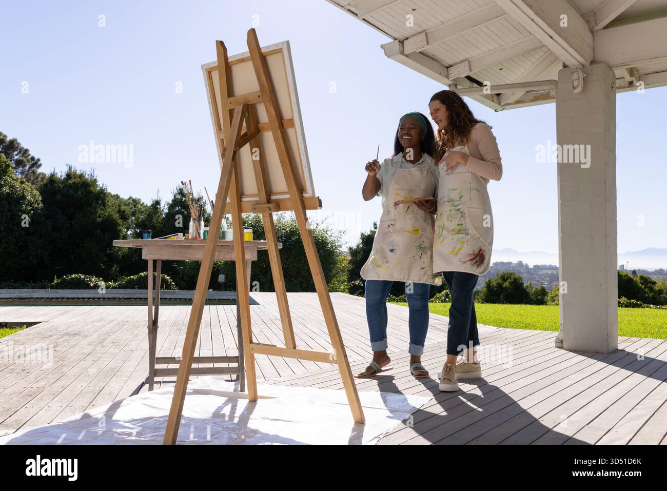 Istruttore afroamericano e studente maturo che dipinge sulla terrazza all'aperto, con cavalletto e tavolozza di pittura Foto Stock